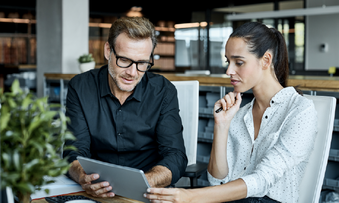 To mennesker sidder og taler sammen på et kontor, mens de kigger på en computer
